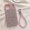 Pink glitter bow iPhone 17 Pro Max case and matching wrist strap in a lifestyle setting